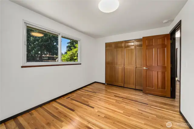 Spacious primary bedroom featuring refinished hardwood floors, a large window for natural light, and an expansive wall-to-wall closet with paneled doors for excellent storage. Neutral finishes and simple lines make this room move-in ready and easy to style as your personal retreat.