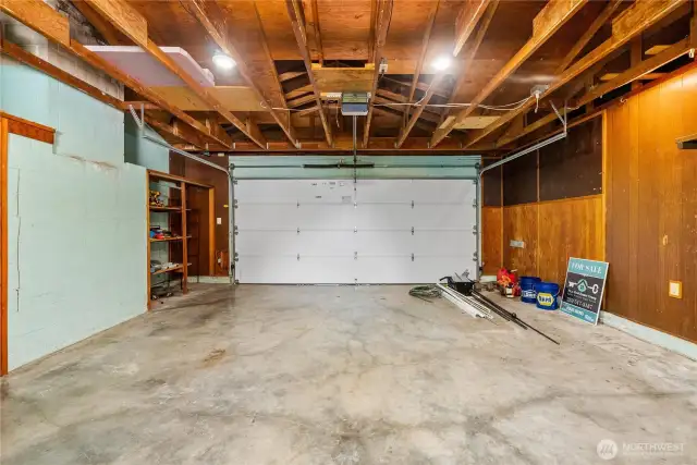 Spacious two-car garage with durable concrete flooring, exposed beam ceiling, and built-in shelving for storage or tools. The newer automatic garage door adds convenience, while the open layout provides plenty of room for vehicles, hobbies, or a home workshop.