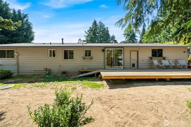 Wide view of the backyard showcasing the home’s exterior and spacious wood deck, perfect for entertaining or relaxing outdoors. Access the dining room through the sliding glass door and the garage through the single door.