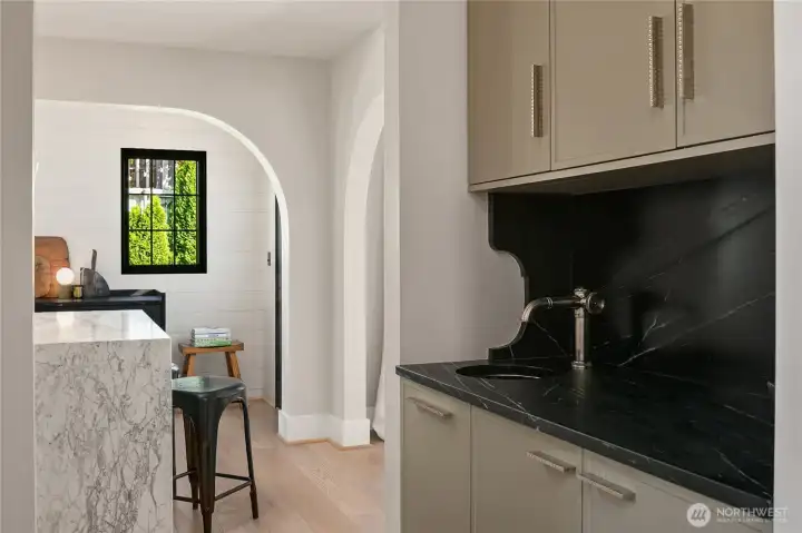 Converted from a former closet, this custom wet bar features a soapstone counter and backsplash paired with Waterworks fixtures. The space is finished with a hammered bar sink, creating a perfect spot for cocktails or coffee service.