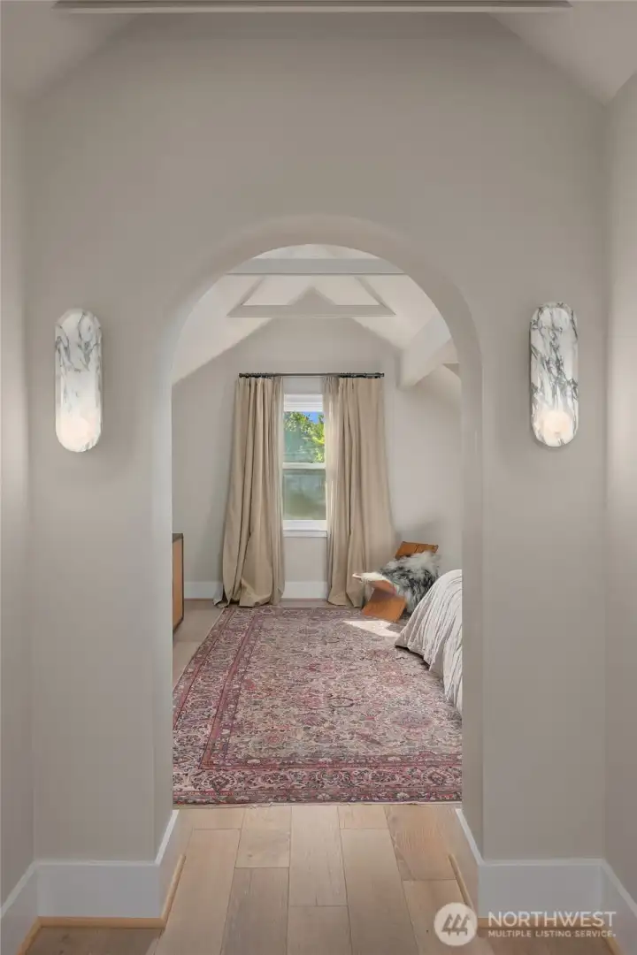 Arched passageways and marble sconces introduce the serene primary suite, where vaulted ceilings and natural light create a calming sanctuary.