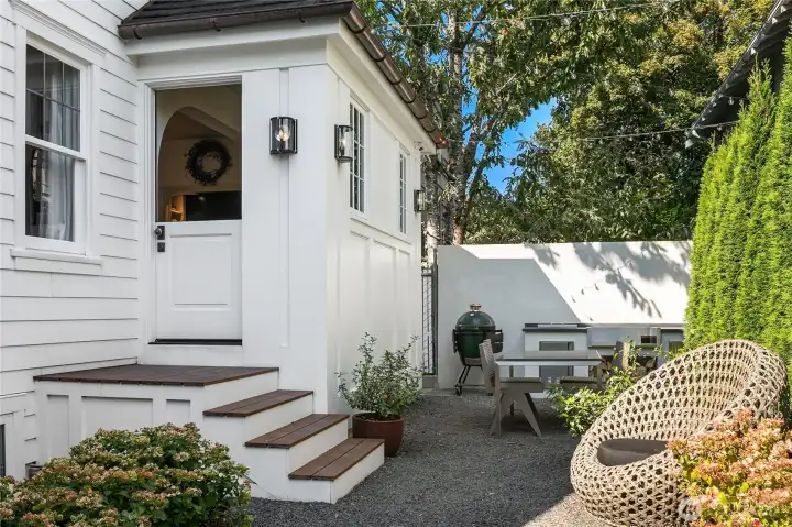 Step through the charming Dutch door to a private garden retreat, complete with a custom-built outdoor kitchen and dining area framed by lush greenery—perfect for summer evenings and weekend gatherings. (Railing, not shown, now installed.)
