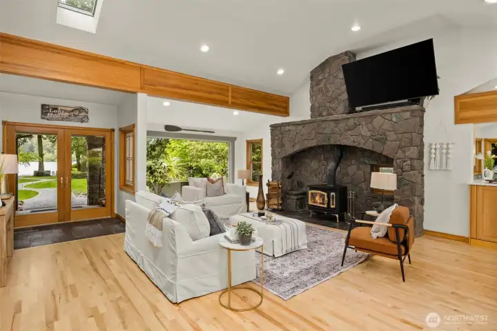 Generous living area with refinished hardwood floors, wood-burning stove, striking rock wall, vaulted ceilings, and exposed beams Generous living area with refinished hardwood floors, wood-burning stove, striking rock wall, vaulted ceilings, and exposed beams