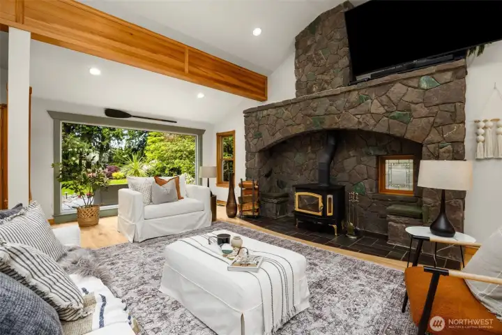 Generous living area with refinished hardwood floors, wood-burning stove, striking rock wall, vaulted ceilings, and exposed beams Generous living area with refinished hardwood floors, wood-burning stove, striking rock wall, vaulted ceilings, and exposed beams