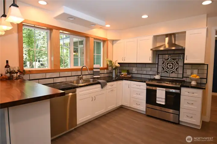 The heart of the home ~ this designer kitchen showcases sleek counters, SS appliances, custom tile backsplash, and a statement gas range alcove.
