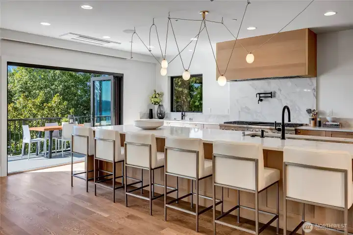 two large NanaWall doors that fold open to create a seamless indoor-outdoor flow. The huge quartz waterfall island, sleek cabinetry, and modern lighting make the space feel bright, open, and perfect for gathering.