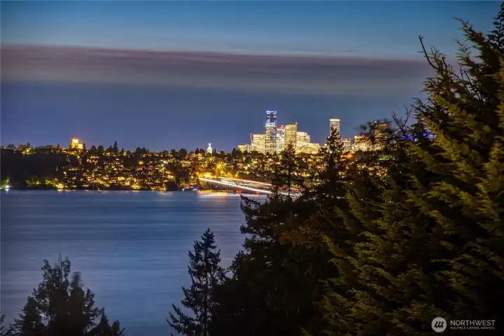 The home captures a stunning nighttime panorama of Lake Washington and the Seattle skyline glowing across the water. Framed by evergreens, the view feels peaceful, private and beautifully connected to the city.