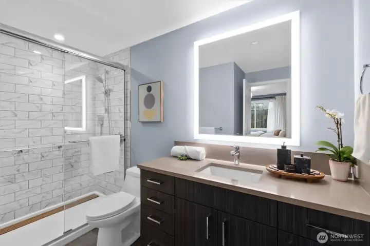 Spacious tiled shower with LED mirror.