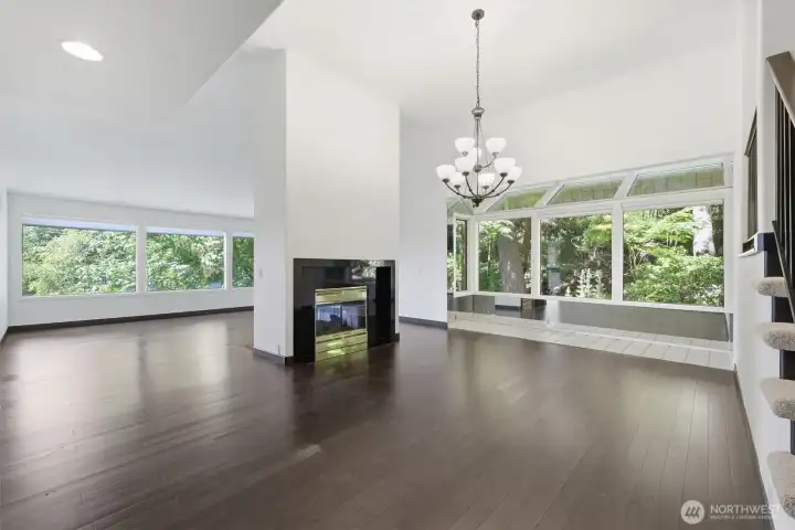 Dramatic open-concept living and dining spaces featuring soaring ceilings, rich hardwood flooring, floor-to-ceiling windows, and a dual-sided fireplace overlooking a private woodland setting. Dramatic open-concept living and dining spaces featuring soaring ceilings, rich hardwood flooring, floor-to-ceiling windows, and a dual-sided fireplace overlooking a private woodland setting.