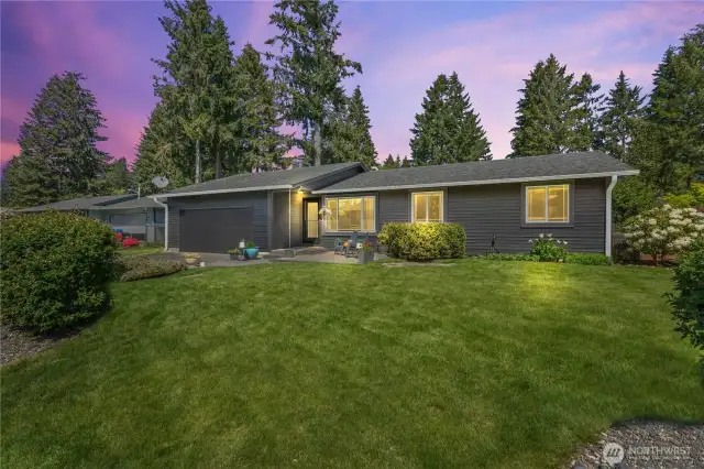 Welcome to 3727 Hoadly Loop SE – This twilight exterior shot highlights the home's beautiful curb appeal, lush green lawn, and freshly painted 2024 exterior. Nestled on a spacious lot in Tumwater, this remodeled rambler stuns with its modern charcoal tones, large picture windows, and cozy evening glow—perfect for showcasing indoor/outdoor lifestyle potential.