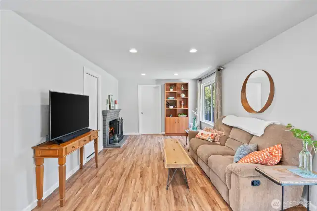 Bright and cozy living room with large picture window overlooking the landscaped yard, recessed lighting, and rich wood-look flooring—perfect for relaxing or hosting guests.