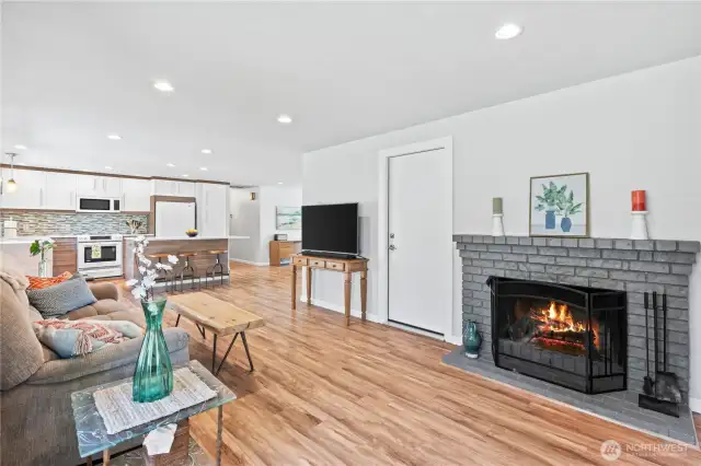 Open-concept layout seamlessly connects the living area to the kitchen, featuring a cozy painted brick fireplace and inviting ambiance with updated recessed lights.