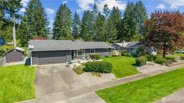 Striking front view highlights a double-car garage, wide driveway, and freshly painted exterior complemented by manicured hedges and a garden shed.
