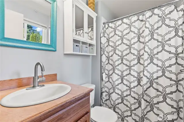 Fresh and functional full bathroom featuring a stylish vanity with updated faucet, built-in wall cabinet for added storage, and a tub/shower combo with modern patterned curtain. Natural light and thoughtful accents add charm to this everyday essential space.