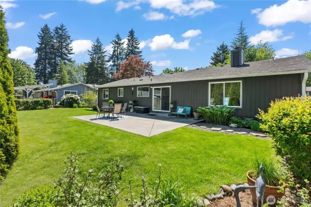 Enjoy seamless indoor-outdoor living with this beautifully maintained backyard featuring a generous concrete patio, ideal for summer BBQs and family gatherings. Surrounded by mature landscaping and privacy trees, this level yard offers ample green space for kids, pets, and entertaining under the Pacific Northwest sky.
