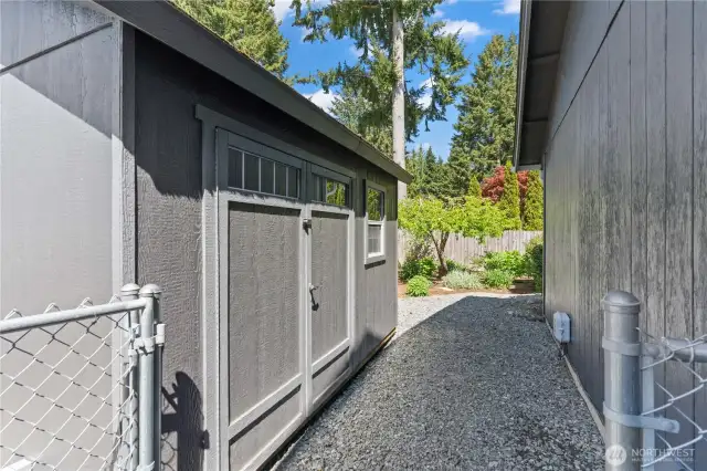 Side yard features a secure gravel walkway leading to a large, windowed garden shed—ideal for organized storage and easy access to tools and equipment.