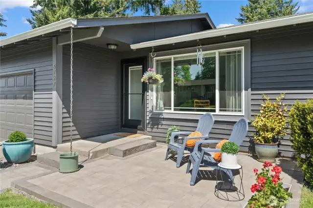 A closer look at the front patio reveals modern pavers, Adirondack seating, and floral accents that enhance the home’s charm. Rain chains and updated trim complete this serene, low-maintenance entryway ideal for enjoying the Pacific Northwest seasons.