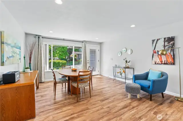 Sun-filled dining area framed by a large picture window and glass door, offering lush front yard views and direct access to the patio—perfect for entertaining or everyday meals.