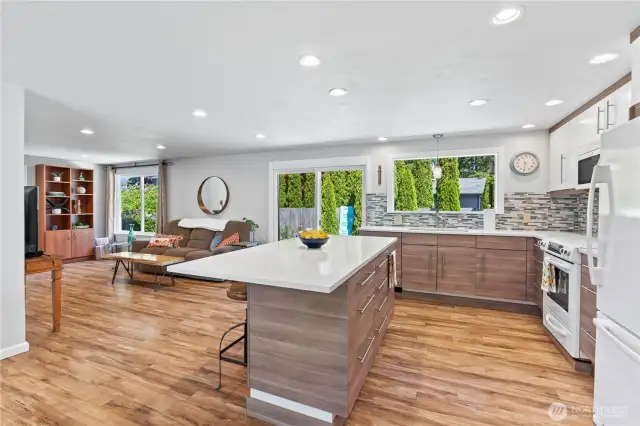 Step into a chef-inspired kitchen featuring a stunning quartz waterfall island, custom soft-close cabinetry, and full tile backsplash. Enjoy open sight lines to the cozy living area and views of the landscaped backyard through oversized windows and a sliding glass door—perfect for entertaining or relaxing in style.