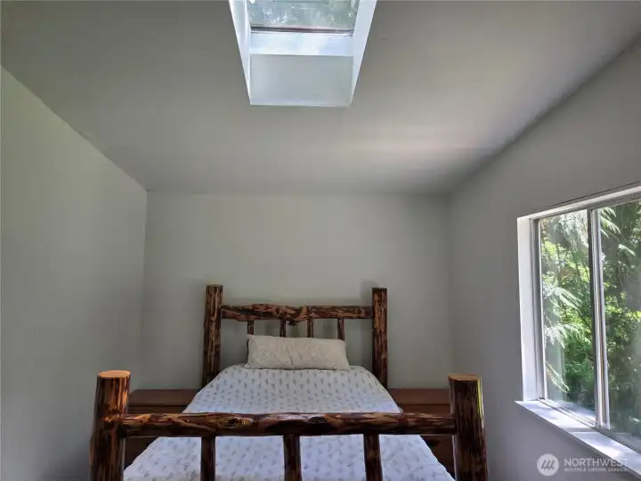 Primary bedroom has skylight for additional lighting. The room is large enough to easily accommodate this queen size bed with end tables.