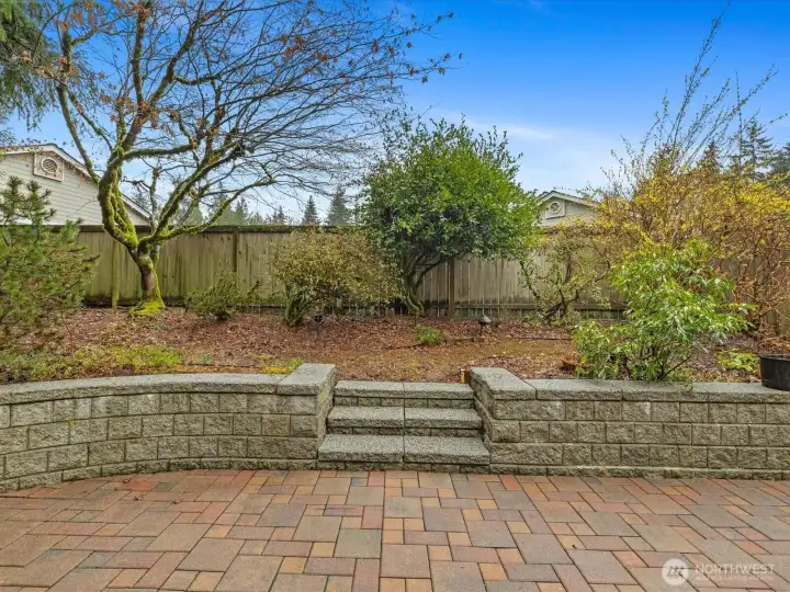 Brick paver patio with stone retaining wall and steps leading to a fully fenced area — a generously sized private outdoor space