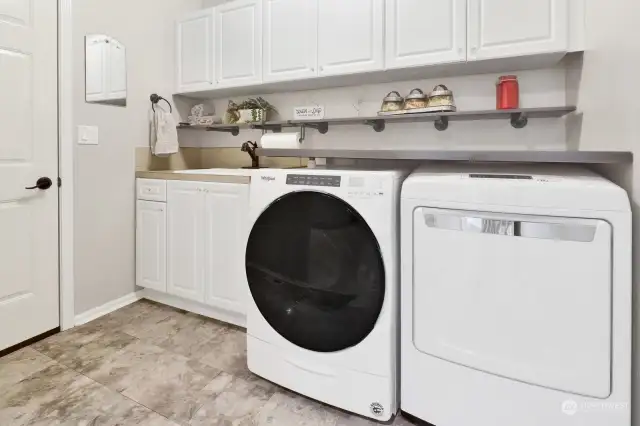 Generous laundry room loaded with cabinets, sink, folding table, coat hooks, and provides access to the garage.