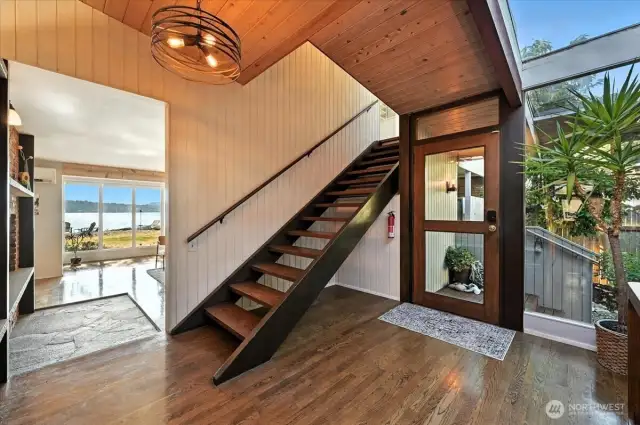 Step into an inviting entry where warm hardwood floors meet expansive floor-to-ceiling windows, offering stunning natural light and gentle glimpses of the shoreline beyond.