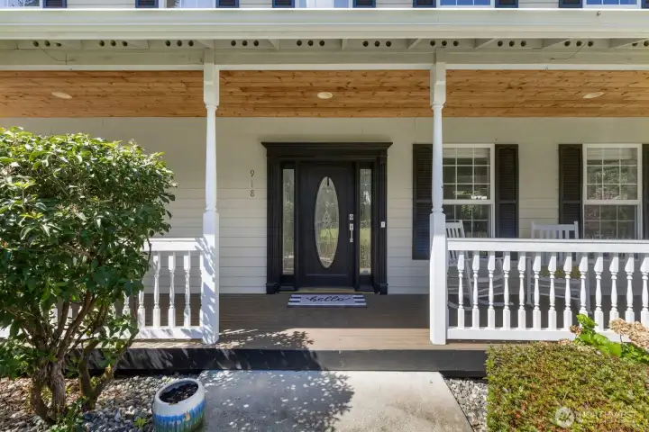Step up to a welcoming covered front porch featuring elegant white railings and ring doorbell.
