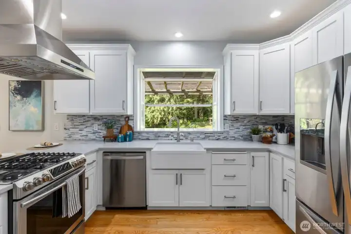 The gourmet chef's kitchen boasts pristine white shaker cabinetry, premium stainless steel appliances, a farmhouse sink, and a stylish glass tile backsplash.