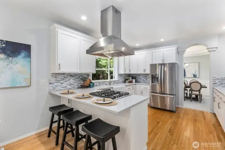 The kitchen features a breakfast bar with seating and a powerful statement vent hood.