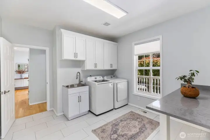 The bright and spacious laundry room is highly functional, offering extensive white cabinetry, a utility sink, and ample counter space.