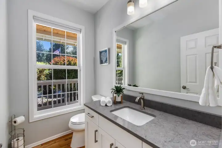 The elegant main-floor powder room features gleaming hardwood floors, crisp white wainscoting, and a modern vanity with quartz countertops and undermount sink.