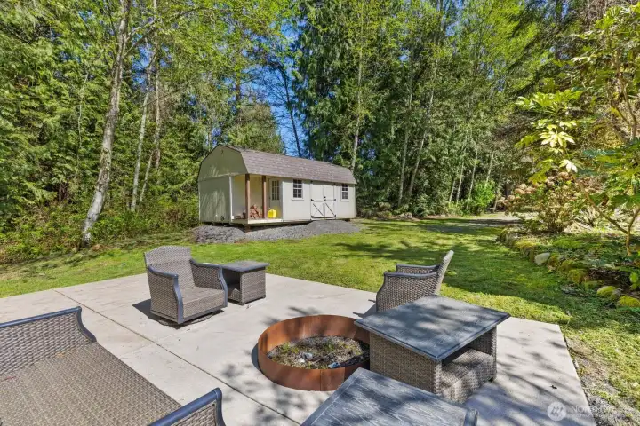 Gather around the cozy fire pit on this inviting outdoor patio, offering lovely views of the expansive lawn and the generously sized shed, perfect for storing your riding lawnmower and tools.
