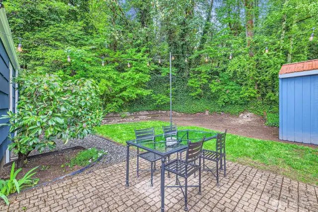 Patio beyond the covered deck with outdoor deck lights. Storage shed and lawn in the background.