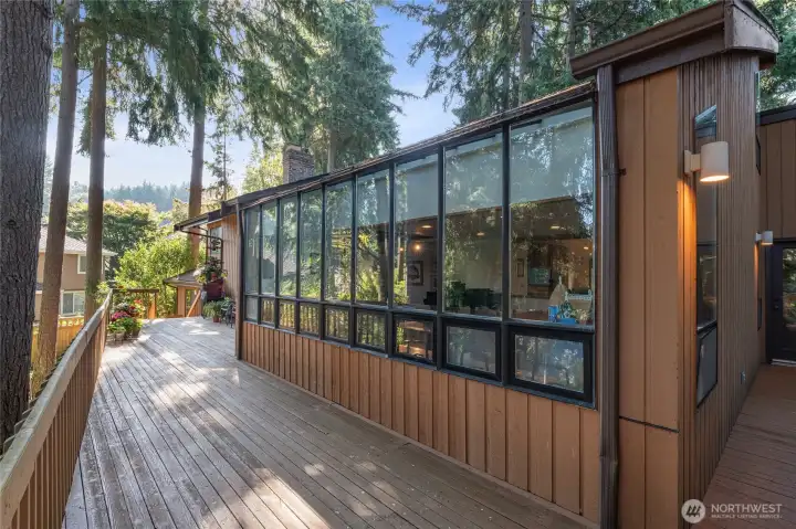 Expansive wraparound deck runs the length of the home, bordered by a striking wall of windows that brings the outdoors in. Surrounded by mature evergreens, this private setting offers generous space for seating, entertaining, and container gardening, all while enjoying serene, tree-lined views.