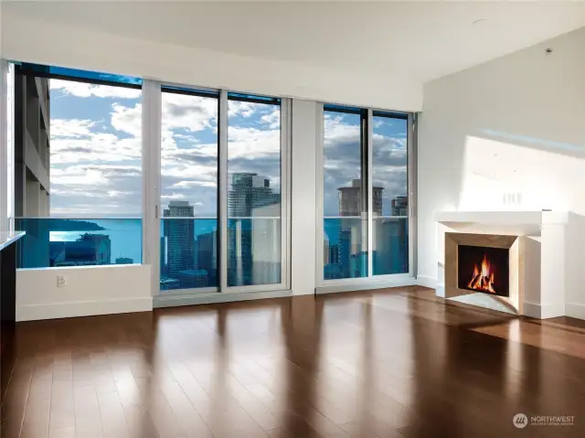 Breathtaking living room, where large expanses of glass and two sliding doors showcase sweeping views of Puget Sound, West Seattle, and the vibrant city skyline.