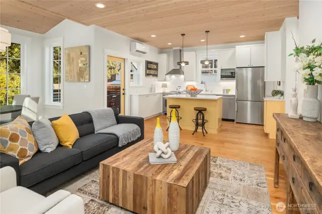 The living room, dining room and kitchen spaces are graced with solid wood floors below and whitewashed pine paneled ceilings above.