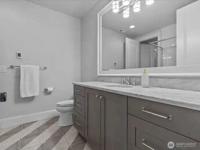 The lower-level en suite bathroom boasts luxurious radiant flooring and elegant marble countertops, enhancing comfort and style.