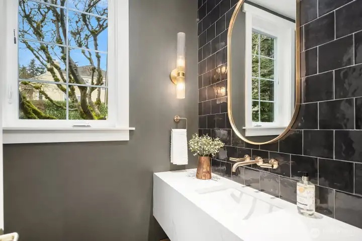 A strikingly designed powder room features dramatic dark tile, a sleek modern vanity, and an eye-catching mirror, a beautifully remodeled and thoughtfully appointed space that makes a lasting impression on every guest. A strikingly designed powder room features dramatic dark tile, a sleek modern vanity, and an eye-catching mirror, a beautifully remodeled and thoughtfully appointed space that makes a lasting impression on every guest.