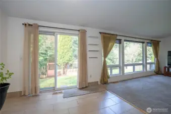 View of the living area from the dining space, featuring a sliding door that opens to the backyard and spacious deck overlooking the Olympic View Park trail system.