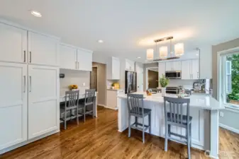 Kitchen includes a built-in desk area with overhead storage and workspace. Seamless transition to adjacent hall and garage access.