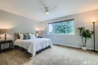 Upper-level primary bedroom with large window and neutral carpet. Ceiling fan provides added comfort year-round.
