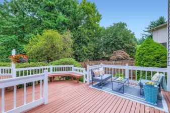 Spacious and freshly refinished wood deck surrounded by mature landscaping and built-in bench seating—ideal for outdoor entertaining or quiet morning coffee.