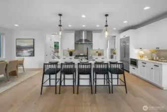 Gourmet kitchen featuring an oversized waterfall island with seating for five, professional-grade appliances, custom cabinetry, and designer tile backsplash. A true centerpiece for the home.