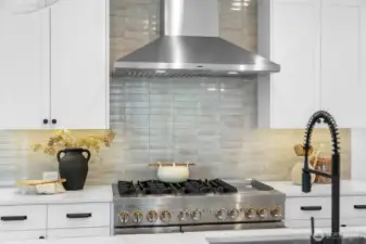 Professional-grade gas range with stainless steel hood, quartz counters, and artisan tile backsplash. A chef’s dream setup for culinary creativity.