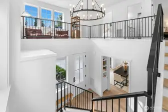 Dramatic two-story entry with open staircase, metal rail detail, and upper-level lounge flooded with natural light. A striking architectural centerpiece of the home.