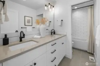 Stylish full bath with dual vanity, quartz counters, subway tile tub surround, and modern matte black fixtures.