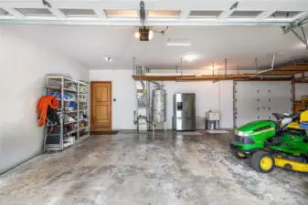 Massive 4-car garage with pass-through garage in the back right. Riding mower included! The kitchen is on the back left. Second refrigerator/freezer provides space for beverages, holiday leftovers, and more. Note the racks hanging from the ceiling; they provide additional storage space for seldom-used items. The shelving on the left of the door will stay.