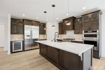 A chef's kitchen with JennAir appliances, pantry, double oven and gas range, beverage fridge, quartz counters, and Huntwood cabinets. Warm, yet bright and inviting.