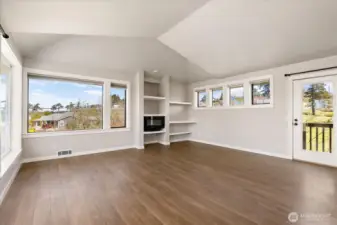 The far end of the living room has shelving nooks with an electric fireplace. To the right is the backdoor.